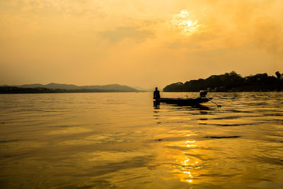 Silhouette man in boat on lake against sky during sunset