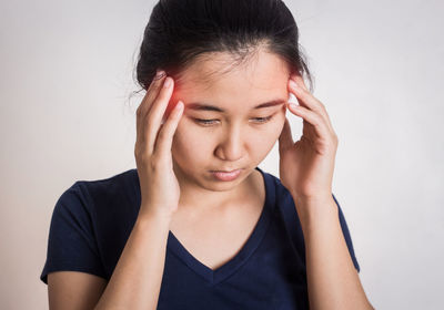 Young woman with headache standing against white background
