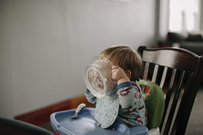 Baby boy eating food while sitting on high chair at home