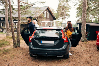 Male and female friends disembarking from car with cottage in background