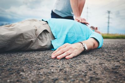 Midsection of man resuscitating friend lying on road