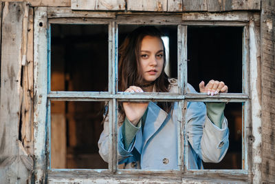 Girl looks out the window from an old wooden house