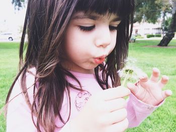 Close-up of cute girl blowing dandelion in park