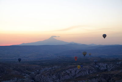 Hot air balloon flying over mountains against sky during sunset
