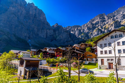 Houses by buildings and mountains against blue sky