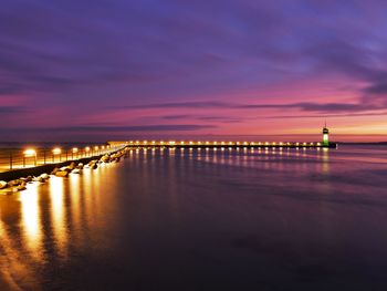 Illuminated pier over sea against sky at sunset