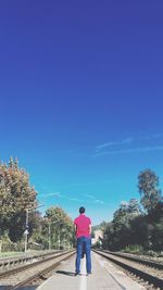 Rear view of man on rail road against blue sky