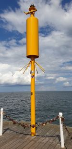 Yellow pole by sea against sky