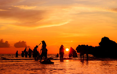 Silhouette people on beach against sky during sunset