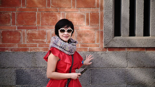 Portrait of mature woman wearing sunglasses while standing against wall