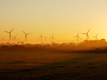 Windmills on field against sky during sunset