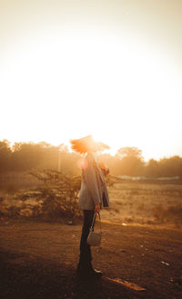 Rear view of woman walking on field against sky during sunset
