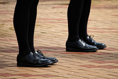 Low section of people in black shoes and socks standing on footpath