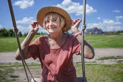 Portrait of smiling woman sitting on swing against sky