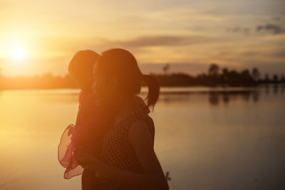 Woman standing by lake against sky during sunset