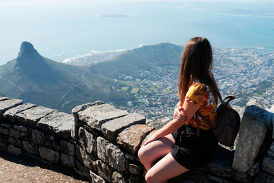 Woman sitting on retaining wall over mountains