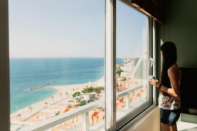 Side view of woman looking at sea through window