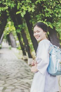 Portrait of smiling woman walking with backpack on footpath