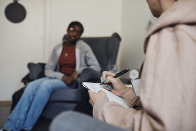 Non-binary counselor writing while discussing with female student in school office