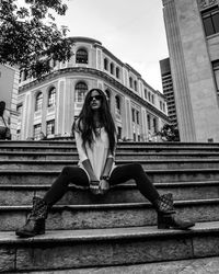 Woman sitting on steps against buildings