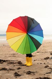 Person holding umbrella on beach against sky