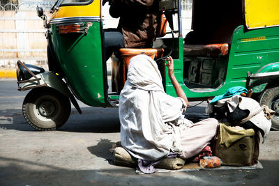 Beggar begging in front of auto rickshaw on street