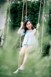 Full length portrait of woman sitting on swing at park