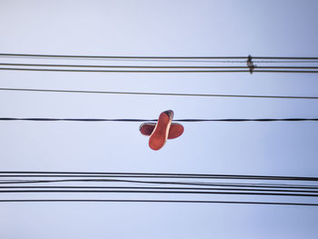 Low angle view of shoes hanging from cables against clear sky
