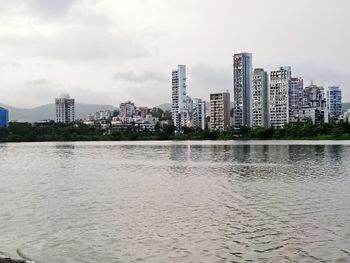 Buildings by river against sky in city