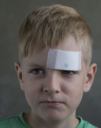 Close-up of boy with bandage on forehead against gray background