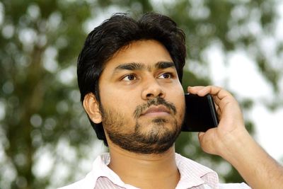 Young man listening to mobile phone while standing against tree