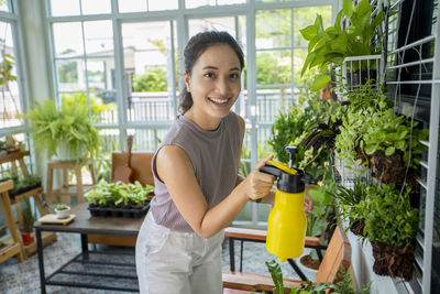 Portrait of smiling young woman watering plants at greenhouse