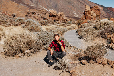 Full length portrait of man sitting on rock