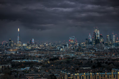 Illuminated buildings in city against cloudy sky