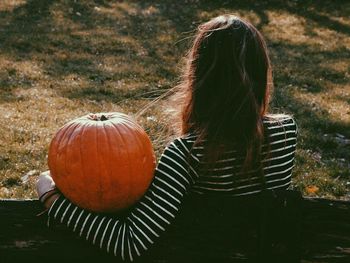 Rear view of woman with pumpkin sitting on field during autumn
