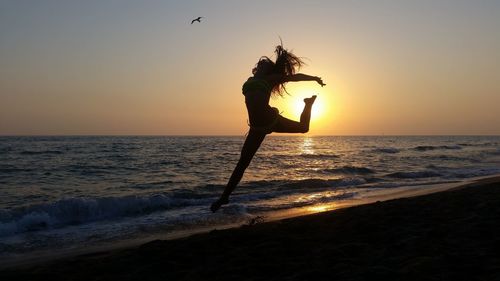 Silhouette woman jumping at beach against sky during sunset