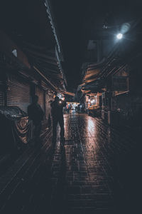 Rear view of man walking on illuminated street at night