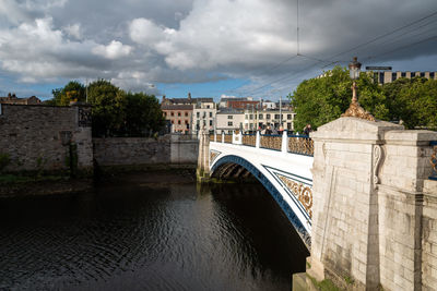 Bridge over river by buildings against sky