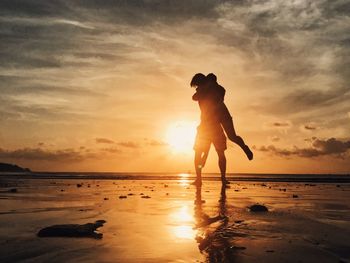 Silhouette of couple embracing while standing at beach against sky during sunset