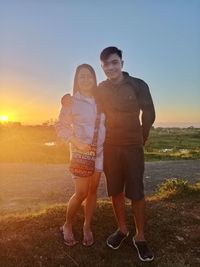 Full length of couple standing on land against sky during sunset
