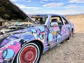 Graffiti on old abandoned car against sky