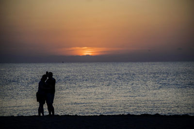 Silhouette couple taking selfie at beach against sky during sunset