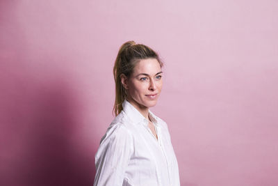 Smiling businesswoman standing against pink background