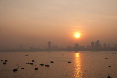 Scenic view of sea by buildings against sky during sunset 