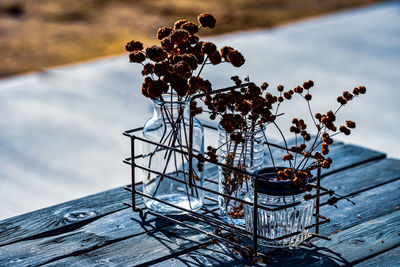 Rustic still life of dried brown flowers in glass jars inside vintage wire rack on wood tble