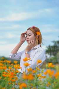 Young woman with flowers on field against sky