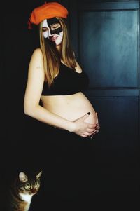 Pregnant woman with painted face standing at home during halloween