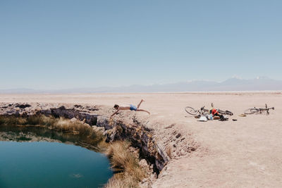 Shirtless man jumping in lake at desert