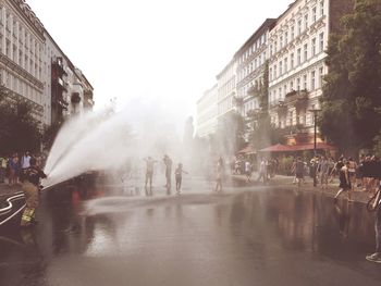 Large group of people enjoying on street with firefighter spraying water