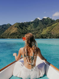 Rear view of woman sitting by swimming pool against sky